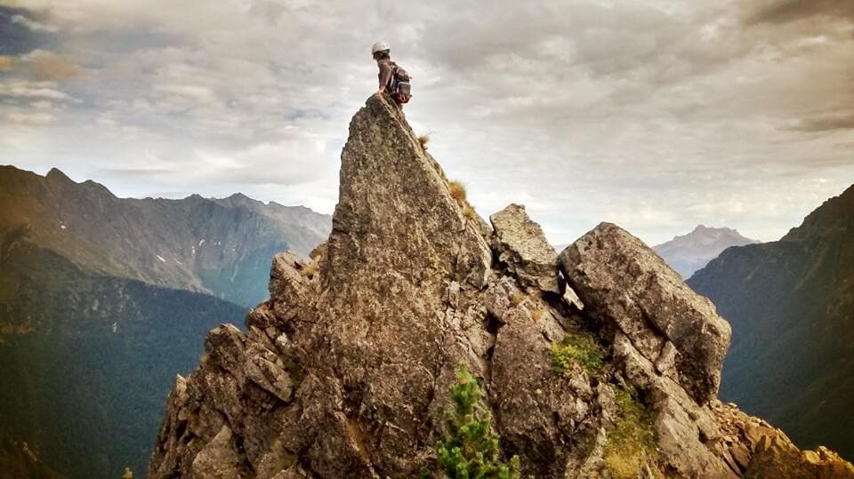  Fabien, un ami d'Anthony, le propriétaire du site, assis au sommet d'une haute roche pointue, dos à la caméra, au sommet d'une montagne, dans les Alpes Française
