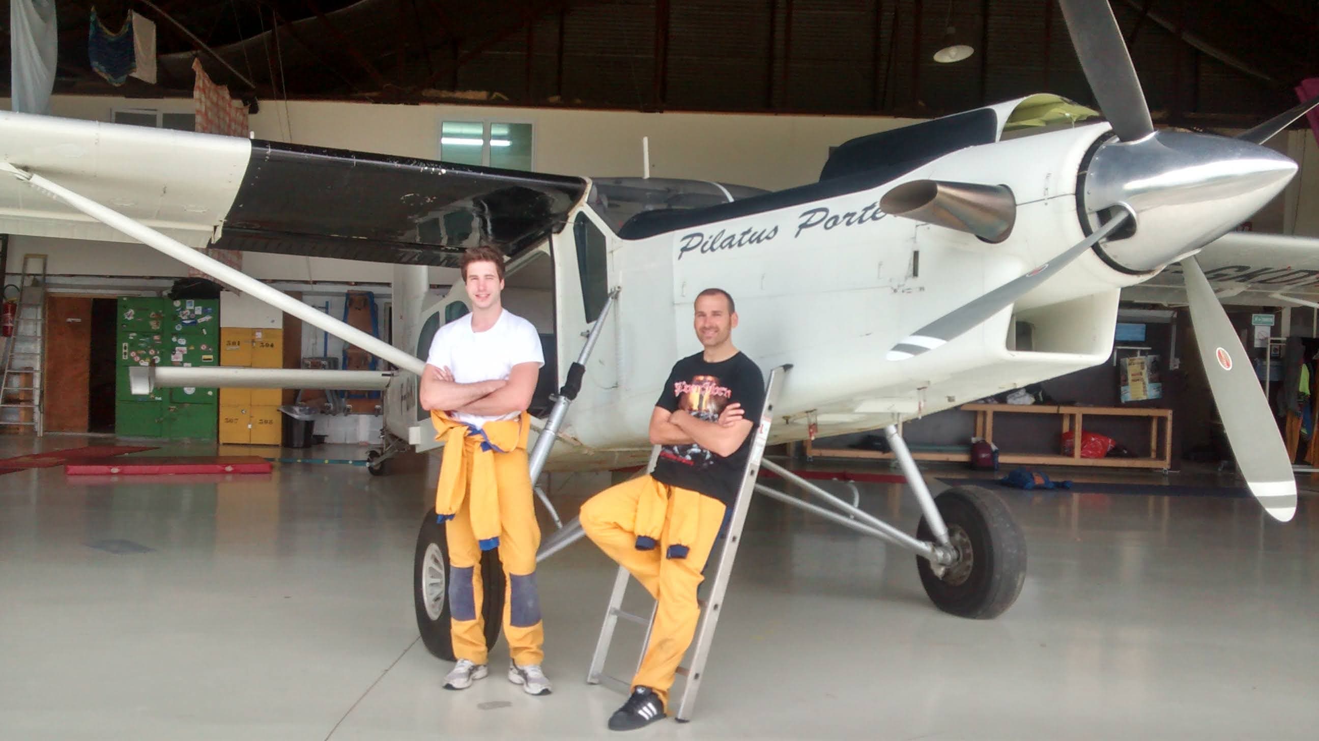 Photo d'Anthony, le propriétaire du site, et son ami Yann, en tenues d'entrainement de parachutisme, devant un avion de petite taille, utilisé pour le saut en parachute
