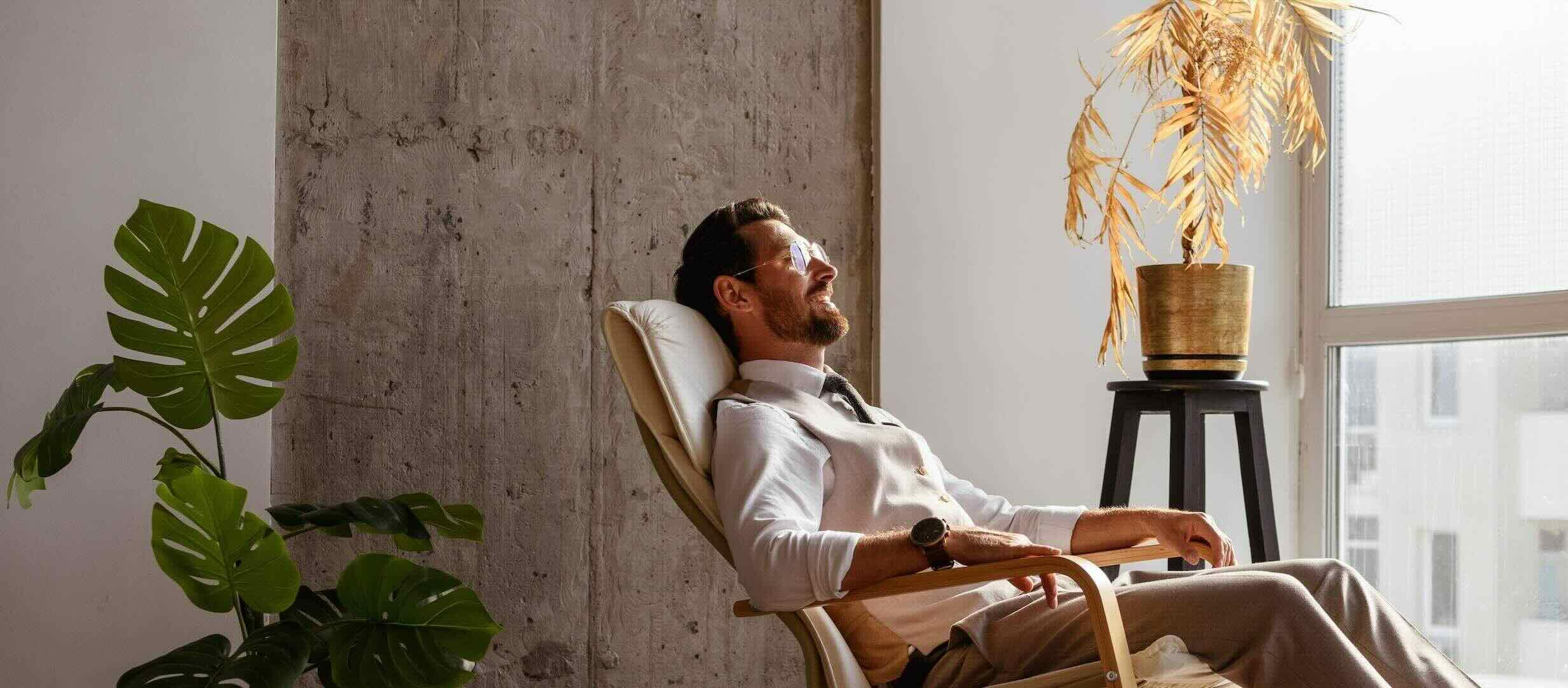 White male laying back on a wooden lounge chair, wearing glasses, relaxing with eyes closed, and wearing a watch