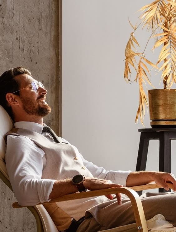 Homme blanc allongé sur une chaise longue en bois, portant des lunettes, se relaxant les yeux fermés et portant une montre