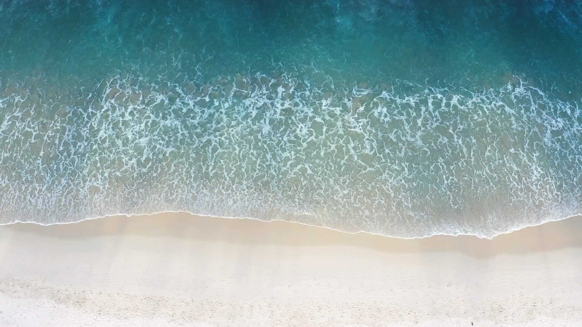 Une vue d'en haut, d'une plage, avec des vagues d'eau d'un bleu profond s'écrasant doucement sur le sable